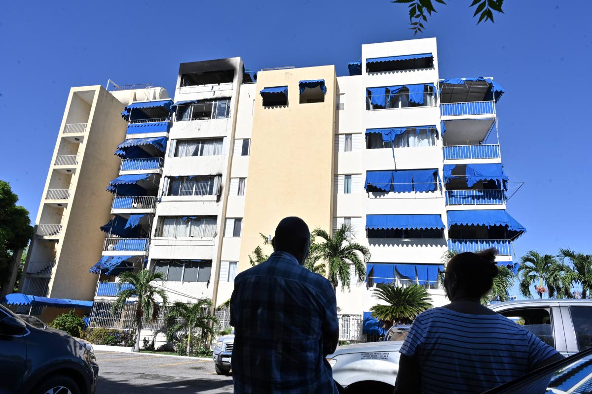Residents of Gallery Apartments on Oxford Road in New Kingston looking at the burnt section of the complex, where 70-year-old Bill Barnes lost his life in an early morning fire on Thursday.