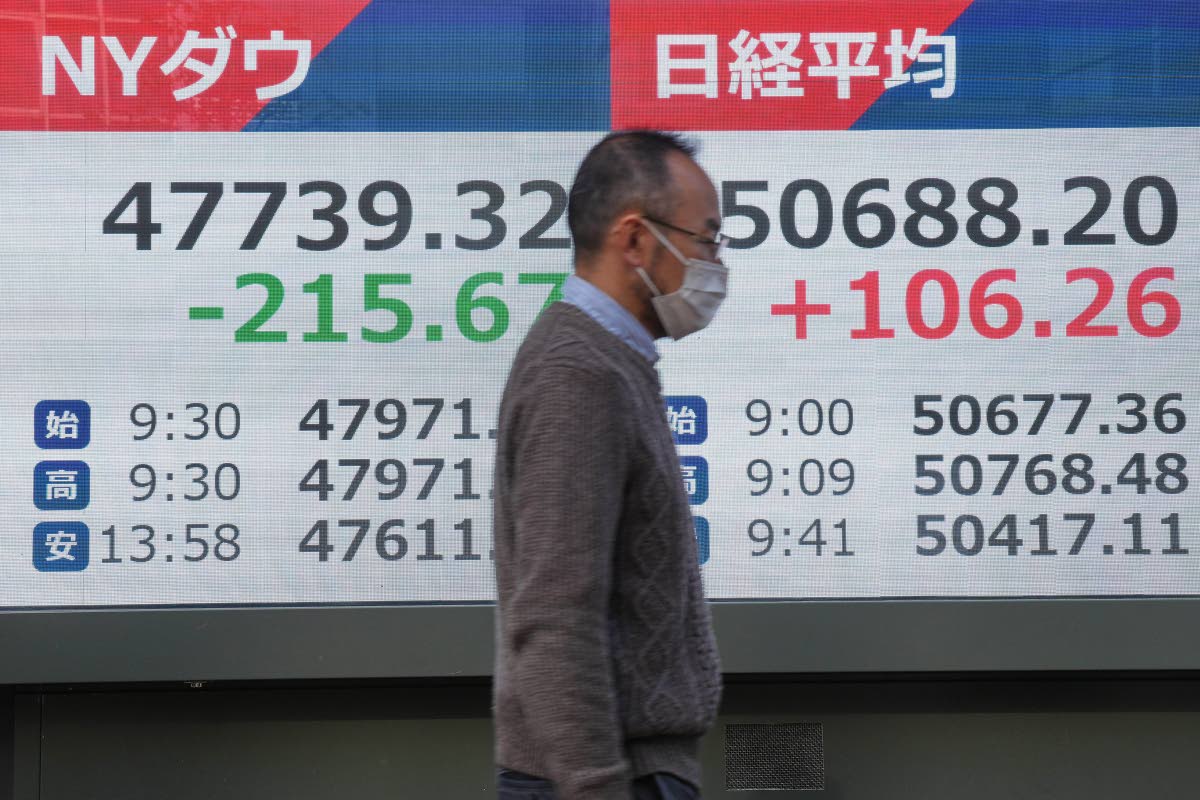 A person walks in front of an electronic stock board showing Japan’s Nikkei and New York Dow indexes at a securities firm Tuesday, Dec. 9, 2025, in Tokyo. (AP Photo)