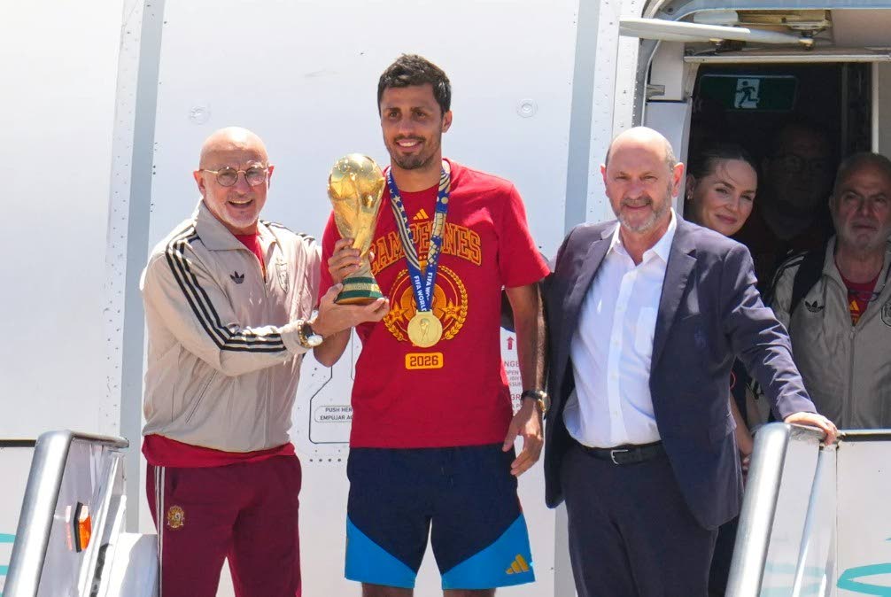 Spain's Rodrigo Hernandez holds the World Cup trophy alongside Spain head coach Luis de la Fuente, left, and Royal Spanish Football Federation President Rafael Louzan as they arrive at Madrid airport on Monday, July 20, 2026, after Spain defeated Argentina