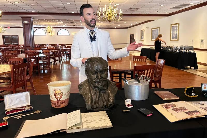 Auctioneer Jonathan Klunk gestures to a display of personal items owned by KFC founder Harland Sanders, Wednesday, July 22, 2026, in Shelbyville, Ky. (AP Photo/Dylan Lovan)