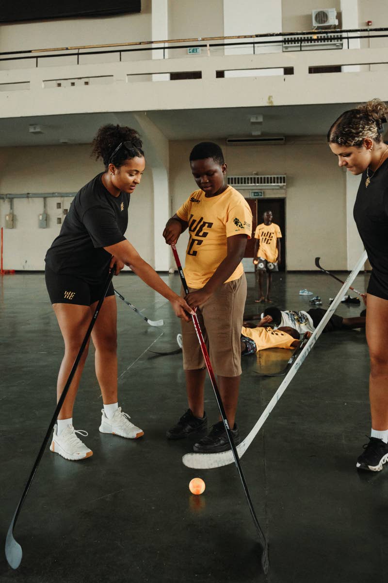 This image provided by the Women of Color Hockey Collective shows WCHC founder Saroya Tinker (left) and University of Delaware player Katelynn Charlton (far right) work with a participant during a hockey clinic inside the Jamaican National Stadium in Kings