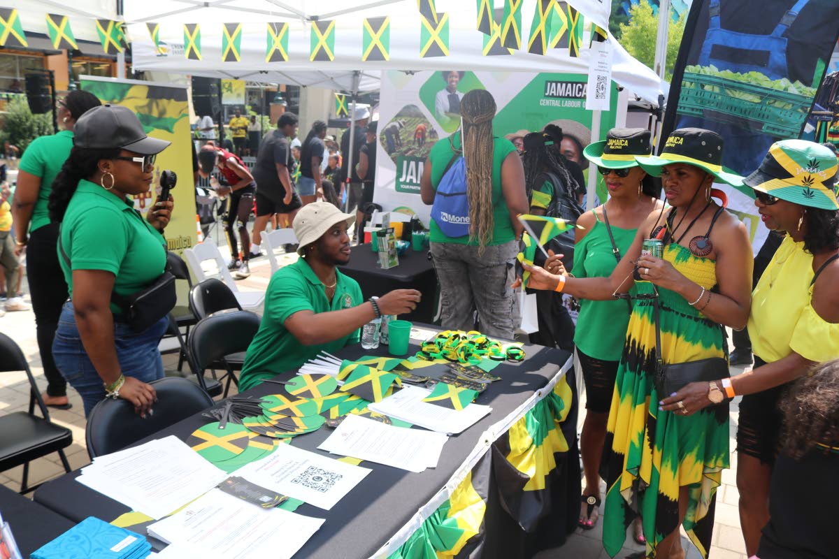 Patrons collect flags and interact with Jamaican Embassy staff members Kasceme Blackwood (right) and Natasha Forrest (left) at the Embassy’s booth during Jamaica Fest at Veterans Plaza in Silver Spring, Maryland, on Sunday, August 9.