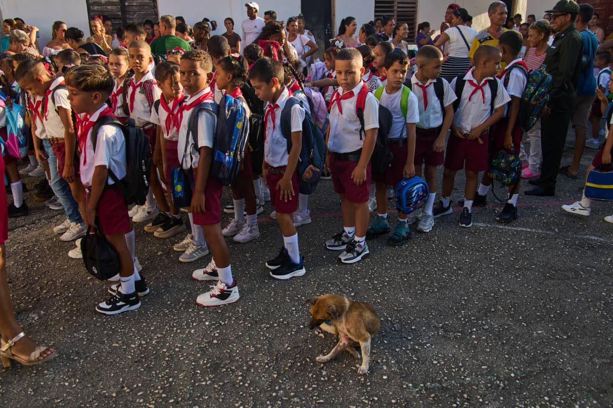 Children line up for their national anthem in the school courtyard where a stray dog sits by on the first day back to school in Minas, Cuba's Havana province, Tuesday, Sept. 1, 2026. (AP Photo/Ramon Espinosa)