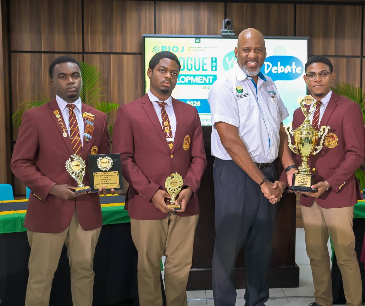 Director General at the Planning Institute of Jamaica (PIOJ), Dr Wayne Henry (second right), presents the winning trophy to Wolmer’s Boys’ School team member Apollos Joiles (right), at the PIOJ’s Dialogue for Development 2026 Youth Debate Competition
