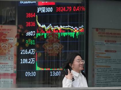AP
A woman passes by a stock index at a brokerage in Beijing in May 2025. 