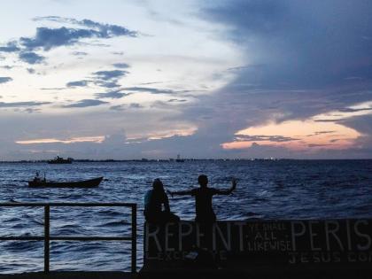 People sit on the seawall as the sun sets in Georgetown, Guyana, November 19, 2024.