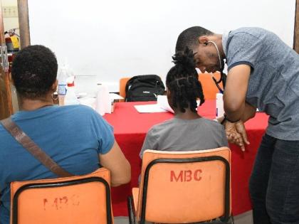 Dr Ryan Haynes, UTech, Jamaica Medical Centre, checks the vitals of a youngster (centre) as her guardian (left) observes during the UTech, Jamaica Health and Services Fair held on Thursday, July 16, 2026, at the Mona Baptist Church.