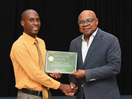 Randell Gordon (left), a recent beneficiary of the East Central St James Scholarship and Welfare Fund, receives his presentation certificate from Edmund Bartlett, minister of tourism and member of parliament for St James East Central, during the 30th annua