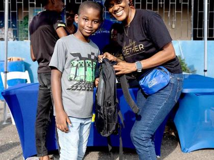 Suzanne Brown (right), administrative assistant, system operations, Jamaica Public Service, presents Ricardo Clarke with a new backpack during a community back-to-school treat at Waterhouse in Kingston on August 30.