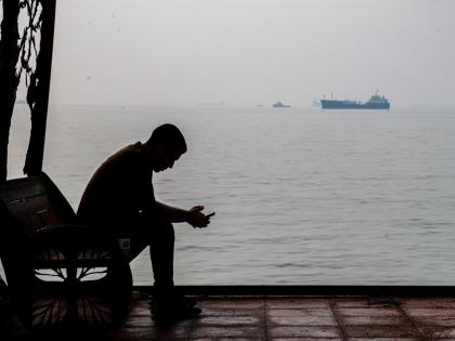 A man checks his cellphone at a waterfront shelter as commercial vessels appear anchored in the Strait of Hormuz off Bandar Abbas, Iran on October 6.