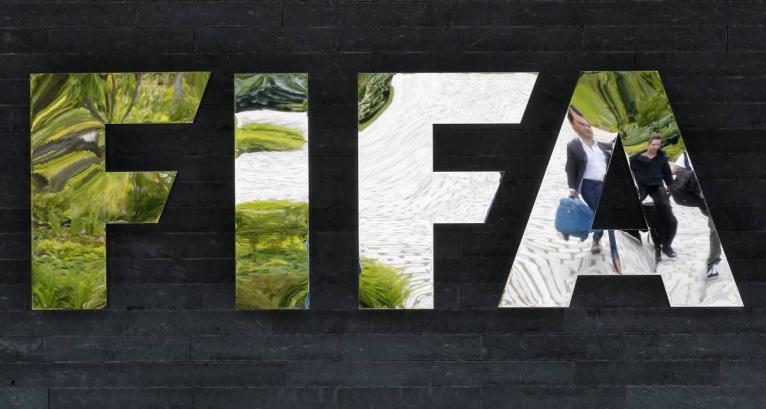 In this May 27, 2015 file photo two persons are reflected in the FIFA logo at the FIFA headquarters in Zurich, Switzerland.