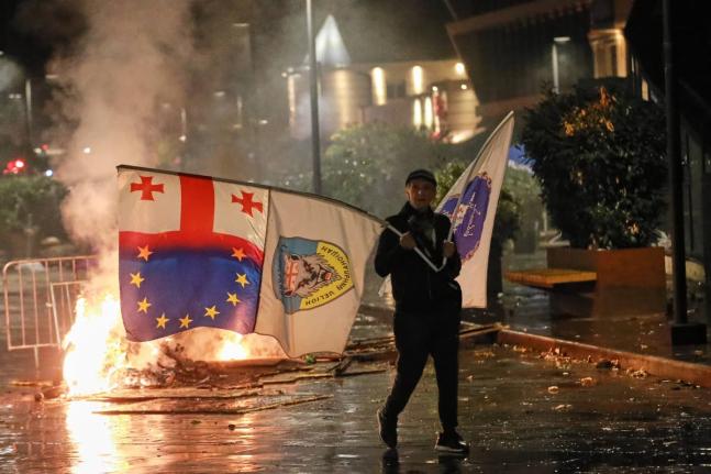A demonstrator with a Georgian national, EU and other flags walks in front of police line during an opposition rally in the city centre of Tbilisi, Georgia.