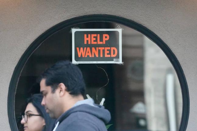 Pedestrians walk past a ‘Help Wanted’ sign posted on the door of a restaurant in San Francisco in April 2023. 