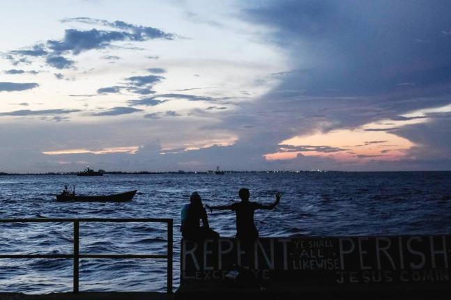 People sit on the seawall as the sun sets in Georgetown, Guyana, November 19, 2024.