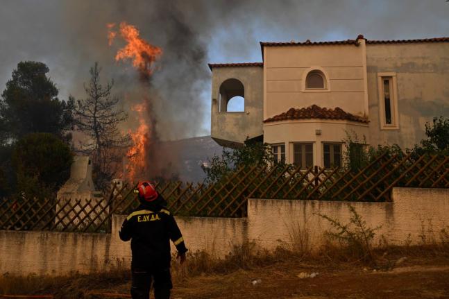 A volunteer firefighter observs a flame rising next to a house during a wildfire near Porto Germeno, northwest of Athens, Greece, Sunday.