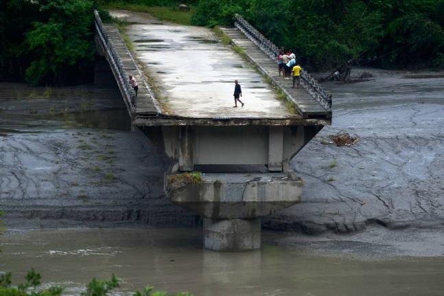 People stand on remnants of a bridge that spanned across the Trishuli River and was washed away in flash floods in Dhading District, Nepal, on Sunday.