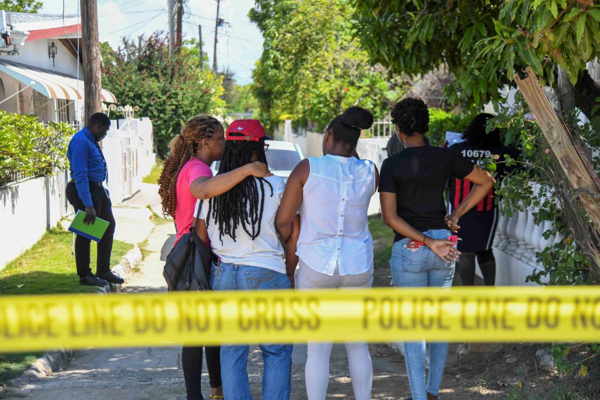 The family of the deceased (from left) Trudyann Bell Williams, niece; Carol Johnson, twin sister; Yasheima Bell, niece; and Toni-Ann Johnson, niece; embrace each other as police inspect a house on Marlin Way in Braeton, Portmore, yesterday. 