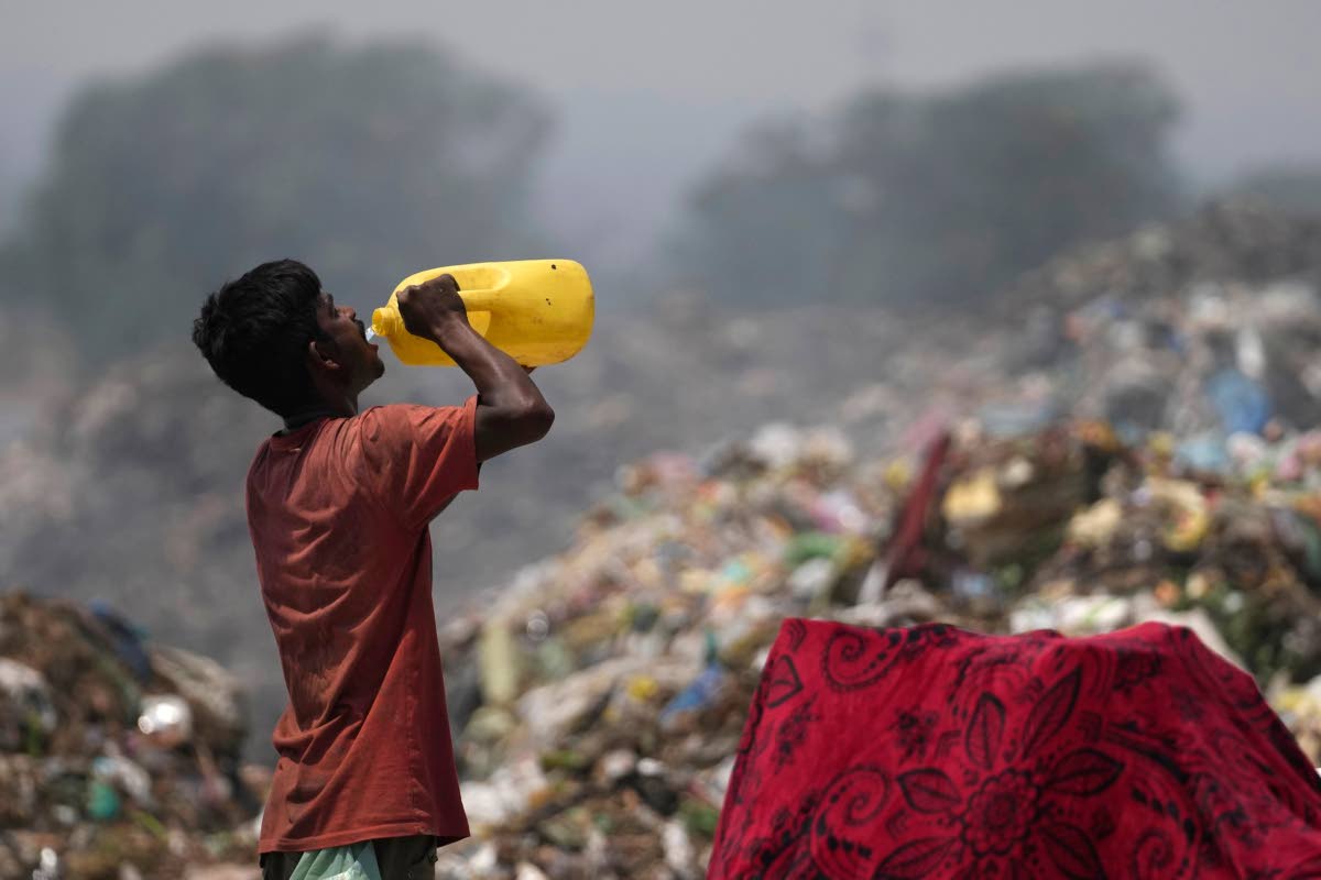 A waste picker drinks water while working during a heat wave at a garbage dump on the outskirts of Jammu, India, on June 19, 2024.