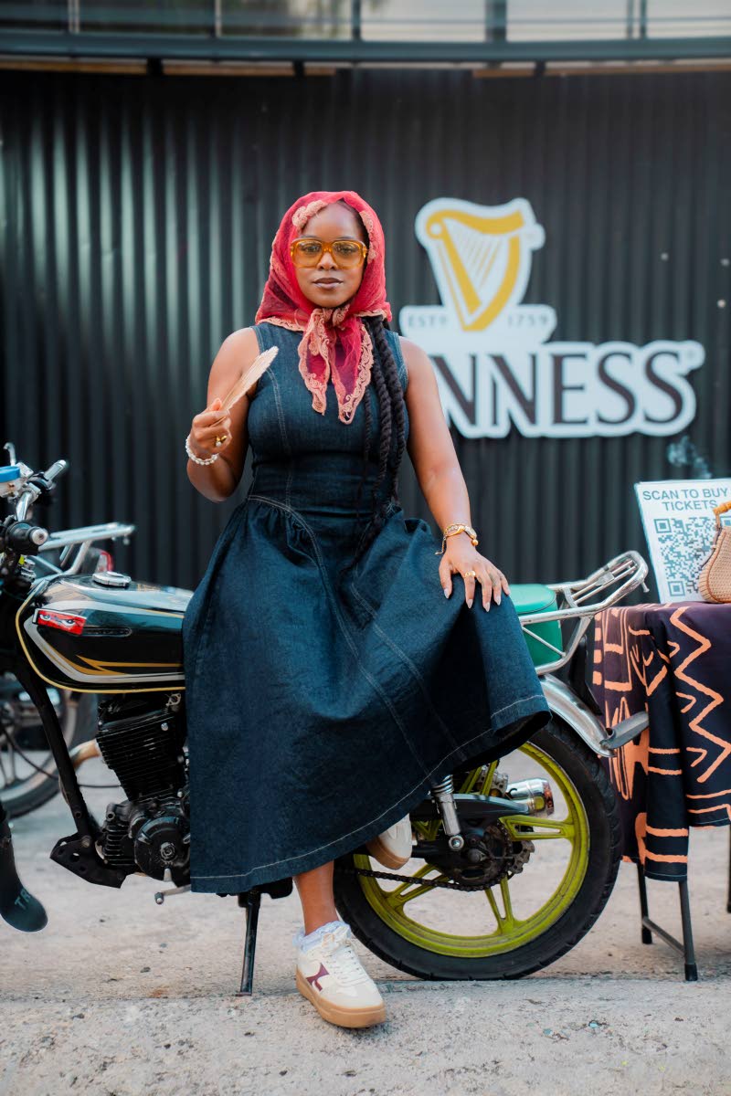 Reggae artiste Khalia sits pretty, rocking a flared denim midi dress, coloured specs and a red head scarf as she keeps cool with a hand-held fan.
