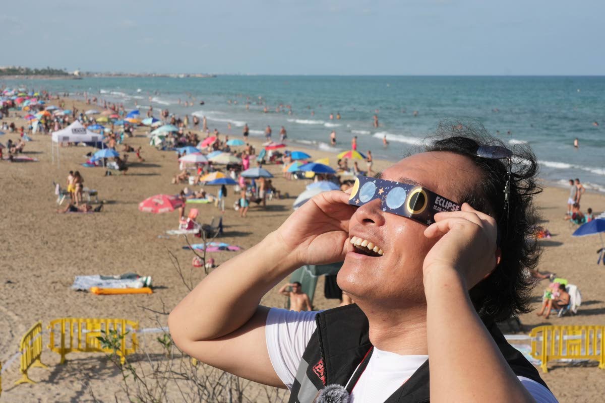 A man wears special eclipse glasses, as beachgoers gather before a total solar eclipse set to begin around sunset, at a beach near Valencia, Spain, Wednesday.