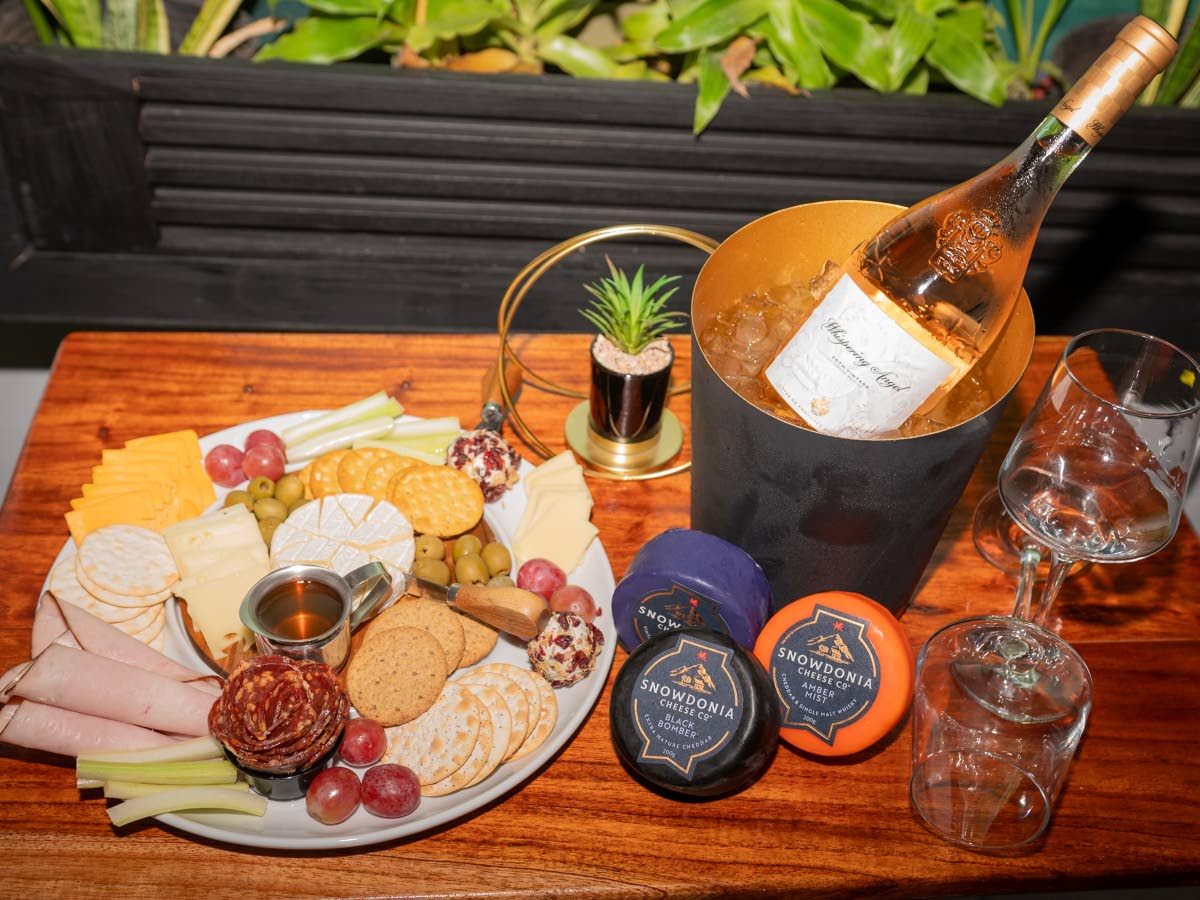 Charcuterie plate featuring a selection of artisan cheeses, cold cuts, crackers and fresh fruit and a bottle of Whispering Angel Rosé.