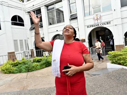 Sophia Lugg, mother of Donna-Lee Donaldson, raises her hand to thank God for showers of rain on leaving the Supreme Court in downtown Kingston after Noel Maitland was yesterday sentenced for the murder of her daughter.