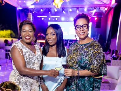 From left: Winsome Gibbs, branch manager for Jamaica, CG United, wears a sleeveless wide-leg jumpsuit as she poses with Donna Brown, chief executive officer of Caribbean Assurance Brokers, in a light blue strapless mini with a plush feather trim, and BCMG 