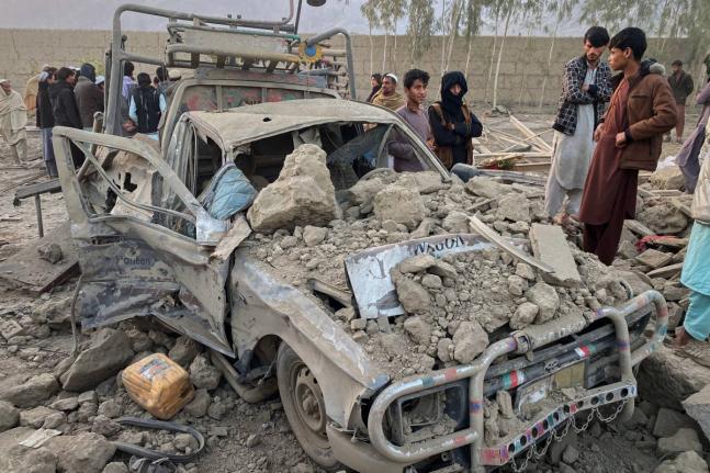 Local residents stand next to a damaged car at the site of a cross-border Pakistani army strike in the Behsud district of Nangarhar province, Afghanistan.