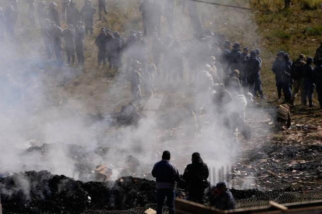 Investigators examine bank notes burned by authorities to prevent people from approaching the scene of a cargo plane that crashed on a highway on February 27, 2026, carrying money, in El Alto, Bolivia.  